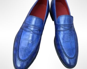 May include: A pair of blue leather loafers with a crocodile texture. The shoes have a red interior and a black sole. The loafers are a slip-on style, suitable for formal or casual wear.