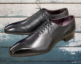 May include: A pair of black leather dress shoes with a glossy finish. The shoes have a classic Oxford design with lace-up closures and a pointed toe. The background is a weathered, blue and white wooden surface.