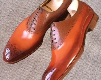 May include: A pair of two-tone leather dress shoes. The shoes feature a glossy, gradient finish, transitioning from a deep brown to a vibrant orange. The uppers have a textured brown leather, with decorative perforations near the toe. The shoes are laced up with brown laces.