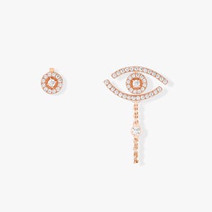 May include: Rose gold earrings featuring a circular stud and an eye-shaped dangle. Both pieces are encrusted with small, sparkling clear stones. The eye design includes a dangling chain with a single stone at the end.