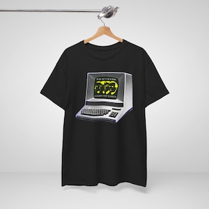 Op de afbeelding: Een zwart t-shirt met korte mouwen en een grafische print van een vintage computermonitor. Het scherm toont de tekst KRAFTWERK COMPUTER WORLD in het geel, samen met een gestileerde gele illustratie van vier gezichten op zwart.