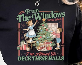 May include: Black sweatshirt with a festive graphic featuring children decorating a Christmas tree, a dog, and the text "From The Windows To The Walls, I'm About To Deck These Halls." A Santa mug is held in the hand.