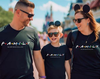 Może przedstawiać: Trzy osoby w czarnych koszulkach z napisem "FAMILY" w kolorowej, stylizowanej czcionce. Koszulki zawierają również imiona "Oliver, Emma, William". Rodzina uśmiecha się i nosi okulary przeciwsłoneczne, spacerując na zewnątrz.