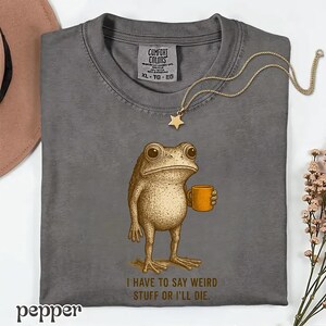 A gray t-shirt with a cartoon frog holding a coffee cup and the text "I HAVE TO SAY WEIRD STUFF OR I'LL DIE."