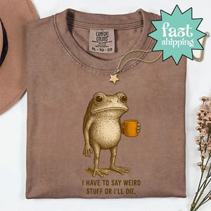 a brown t-shirt with a cartoon frog holding a coffee cup and the text "I HAVE TO SAY WEIRD STUFF OR ILL DIE."