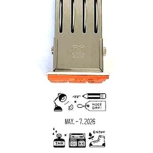 May include: A silver metal date stamp with an orange rubber base. The stamp imprint features a desk lamp, a pencil, a tag with the text NICE DAY!, the date MAY. 7 2026, an ink bottle, a radio, a shoe, and the word ENJOY in black ink.