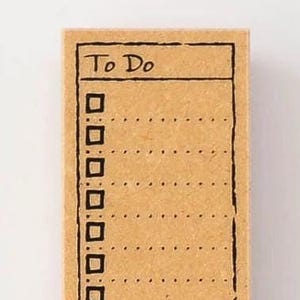 May include: A rectangular rubber stamp with a light brown wooden block base. The stamp features a black ink design of a vertical to-do list with the text To Do at the top, followed by eight square checkboxes and corresponding dotted lines for writing.