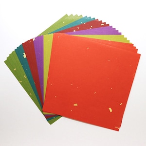 May include: A fan of colorful square paper sheets in shades of red, green, purple, and teal. Each sheet has a textured appearance with gold flecks. The paper is arranged to display the variety of colors and textures.
