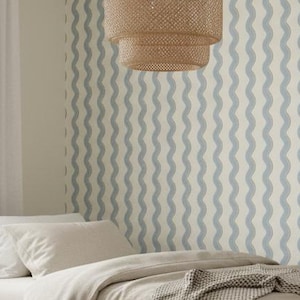 Op de afbeelding: Slaapkamer met een licht houten bed, een beige dekbed en een grijze deken. De kamer heeft een neutraal kleurenschema, een rond tapijt, een houten bijzettafel en een geweven hanglamp. Het behang heeft een blauw golfpatroon.