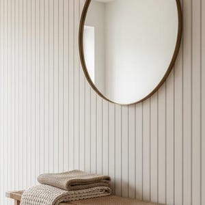 May include: A neutral-toned entryway featuring a wooden bench with a woven seat, topped with folded blankets. Two woven baskets sit below. A round mirror with a gold frame hangs on a vertical-striped wall. The floor is light wood.