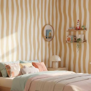 May include: A bedroom interior featuring a light wood bed, bedside table, and chest of drawers. The bed is dressed with pastel-coloured bedding and pillows. The walls have a wavy, striped pattern in cream and gold. A round mirror and a small shelf with decor are also visible.