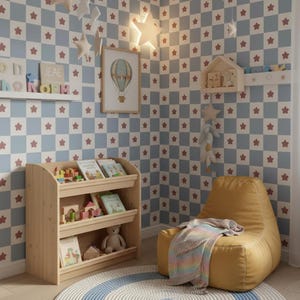 Puede incluir: Una habitación infantil con una estantería de madera clara llena de libros y juguetes. Un puf amarillo con una manta está sobre una alfombra redonda. Las paredes son a cuadros azules y blancos con estrellas rojas, y una imagen enmarcada de globo aerostático cuelga.