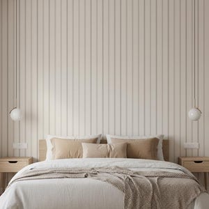 May include: A bedroom scene featuring a bed with a wooden frame, dressed in white linens and tan pillows. A woven throw blanket adds texture. Two spherical pendant lights hang above the bed. The wall is paneled with vertical, light-colored wood.