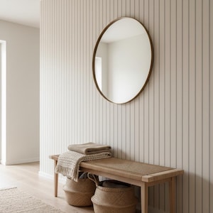 May include: A neutral-toned entryway featuring a wooden bench with a woven seat, topped with folded blankets. Two woven baskets sit below. A round mirror with a gold frame hangs on the striped wall. A rug is on the floor.