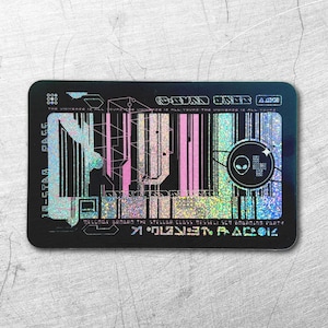 May include: A rectangular black card with a holographic finish featuring stylised geometric patterns, vertical lines, and an alien head icon inside a circle. The card includes text such as 10-STAR PASS and various small, futuristic-looking symbols.