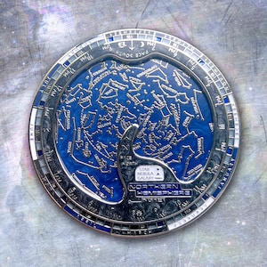 Op de afbeelding: Een ronde metalen sterrenkaart met een diepblauw geëmailleerd centrum voorzien van zilveren sterrenbeeldlijnen en labels. De buitenste ring toont maanden en tijdmarkeringen. De tekst op het object bevat "NORTHERN HEMISPHERE" en "STAR NEBULA GALAXY".