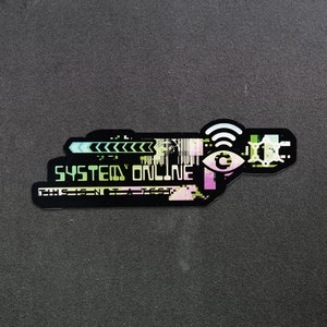 May include: A black and green sticker with a digital design. The sticker says "SYSTEM ONLINE" and features a stylized eye with a wifi symbol above it.