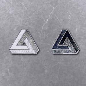 May include: Two triangular enamel pins. One is white and silver, the other is navy and black. Both pins feature a geometric pattern within the triangle shape and have a silver border. The pins are displayed on a textured, gray surface.