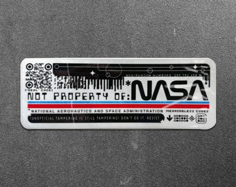 May include: A silver sticker with black text that reads "NOT PROPERTY OF: NASA" and a QR code. The sticker also includes the text "NATIONAL AERONAUTICS AND SPACE ADMINISTRATION" and "MEANINGLESS CODES".