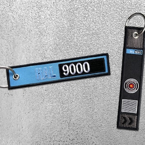 May include: Two keychains, one blue with the text "HAL 9000" and the other black with a red circle and a white rectangle with lines.