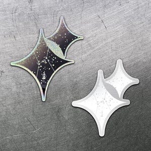 Könnte beinhalten: Zwei sternförmige Aufkleber mit glitzerndem, irisierendem Finish. Einer hat einen dunklen Hintergrund mit weißen Punkten und Linien, der andere ist weiß mit einem ähnlichen Muster. Sie liegen auf einer strukturierten, grauen Oberfläche.