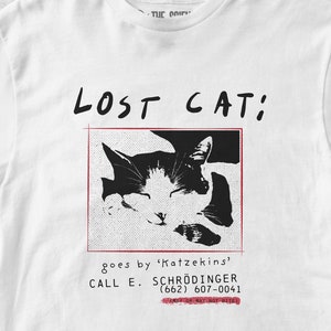 Könnte beinhalten: Ein weißes T-Shirt mit einem Schwarzweißbild eines schlafenden Katers. Der Text "LOST CAT: goes by 'Katzekins' CALL E. SCHRÖDINGER (662) 607-0041 MAY OR MAY NOT BITE" ist auf dem Shirt aufgedruckt.