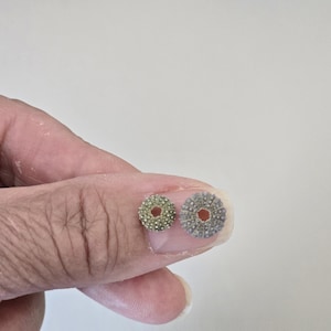 Peut inclure: Deux petits tests d'oursins circulaires avec une surface poreuse et texturée et une ouverture centrale. Un spécimen est vert clair, tandis que l'autre est gris-brun terne. Ces objets marins naturels sont ronds et présentent un motif radial.