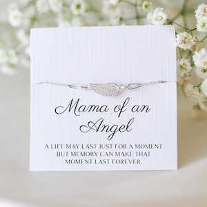 May include: A silver bracelet with a wing charm is displayed on a white card. The card reads "Mama of an Angel" with the text "A LIFE MAY LAST JUST FOR A MOMENT BUT MEMORY CAN MAKE THAT MOMENT LAST FOREVER."