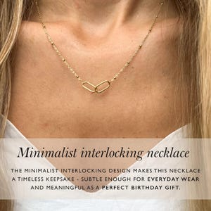 Peut inclure: Un collier doré au design minimaliste. Le collier présente deux pendentifs ovales imbriqués et une chaîne délicate avec de petits accents perlés. Le texte sur l'image se lit "Minimalist interlocking necklace".