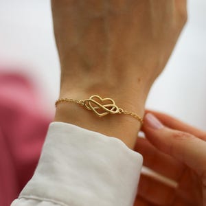Puede incluir: Una pulsera de cadena en tono dorado con un dije central que combina una forma de coraz&oacute;n con un s&iacute;mbolo de infinito. Los delicados eslabones met&aacute;licos se conectan al motivo central, creando un dise&ntilde;o continuo sobre la piel.