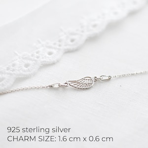 May include: A delicate sterling silver necklace featuring a wing charm. The charm measures 1.6 cm x 0.6 cm. The necklace is displayed on a white background with a lace trim. The text "925 sterling silver" is visible.