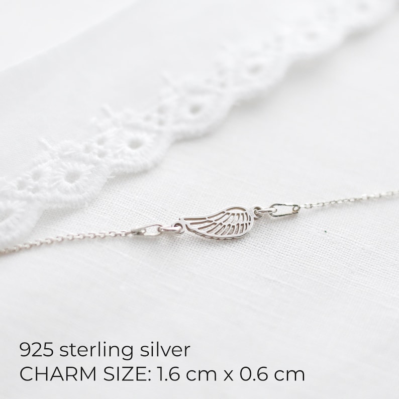 May include: A delicate sterling silver necklace featuring a wing charm. The charm measures 1.6 cm x 0.6 cm. The necklace is displayed on a white background with a lace trim. The text "925 sterling silver" is visible.