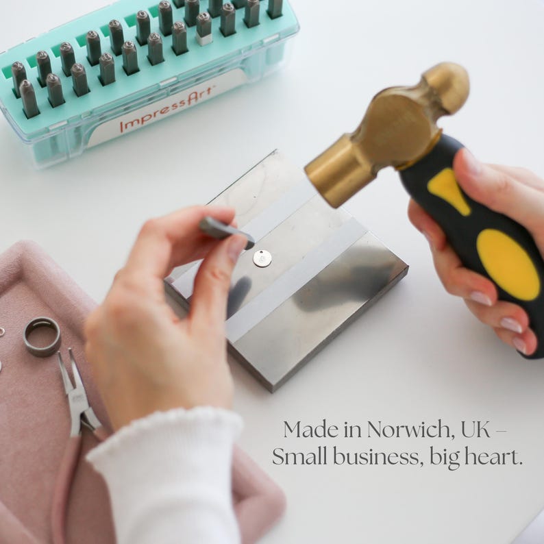 May include: A person using a hammer to stamp a small metal pendant. The image shows tools including a hammer, metal stamps, and a tray with jewelry components. Text in the image reads "Made in Norwich, UK - Small business, big heart."