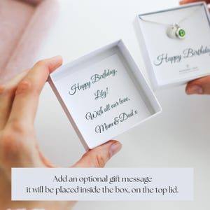 Op de afbeelding: Twee witte geschenkdozen worden opengehouden en onthullen een ketting en een gepersonaliseerde boodschap. De boodschap luidt "Gelukkige verjaardag, Lily! Met al onze liefde, Mama & Papa x." De ketting heeft een zilveren ketting en een groene edelsteen.