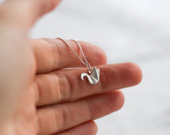 May include: A silver necklace with a delicate origami swan pendant. The necklace is on a white background.