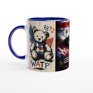 May include: A ceramic mug with a dark blue handle and interior. The exterior features a graphic of a teddy bear wearing a blue, white, and red scarf, the text 1872, and the letters WATP. The design also includes a dark, textured stadium scene.