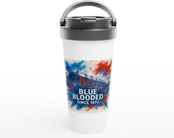 Puede incluir: Taza de viaje blanca con asa y tapa negras. La taza presenta un diseño con salpicaduras de pintura azul y roja y una ilustración de un edificio. El texto en la taza dice "BLUE BLOODED SINCE 1872."