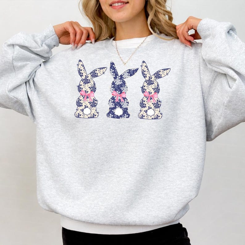Puede incluir: Una sudadera gris claro con tres dise&ntilde;os de conejos. Cada conejo est&aacute; decorado con un estampado floral azul y un lazo rosa. La sudadera es de estilo casual y c&oacute;modo.