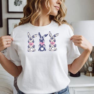 Puede incluir: Camiseta blanca con tres dise&ntilde;os de conejos. Cada conejo tiene un estampado floral azul y blanco con un lazo rosa. Una prenda casual para primavera o Pascua.