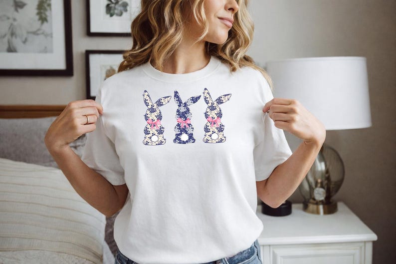Puede incluir: Camiseta blanca con tres dise&ntilde;os de conejos. Cada conejo tiene un estampado floral azul y blanco con un lazo rosa. Una prenda casual para primavera o Pascua.