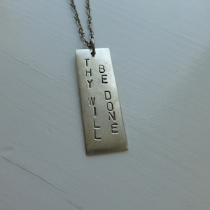 May include: A silver necklace with a rectangular pendant that reads "Thy Will Be Done".
