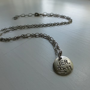 May include: A silver necklace with a round pendant that says "JER. 2011" on it.