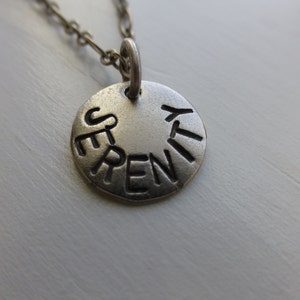 May include: Silver necklace with a round pendant that says "Serenity" in a circular design.