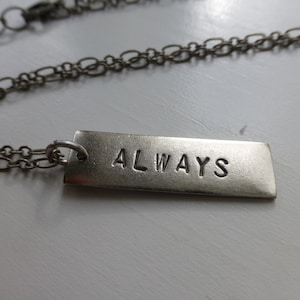 May include: A silver chain necklace with a rectangular pendant that says "ALWAYS" in a simple font.