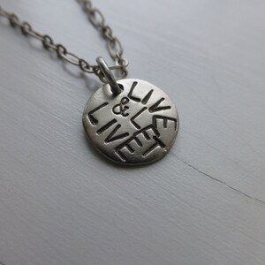 May include: A silver necklace with a round pendant that says "Live & Let Live" in a circular design.