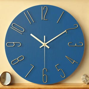 May include: A round wall clock with a deep blue face and gold-colored numerals and hands. The clock has a minimalist design, with a textured surface and a simple, elegant aesthetic. The clock measures approximately 12 inches in diameter.