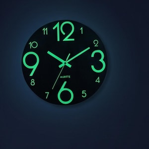 Könnte beinhalten: Eine runde Wanduhr mit schwarzem Zifferblatt und leuchtend grünen Zahlen und Zeigern. Die Uhr verfügt über große, leuchtende Ziffern für die Stunden 12, 3, 6 und 9 sowie kleinere Ziffern für die restlichen Stunden. Der Markenname AURITE ist in Weiß aufgedruckt.