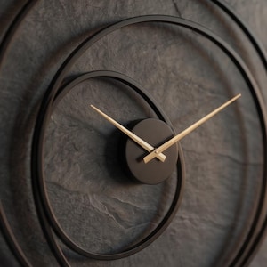 May include: A modern wall clock with a black face and gold-colored hands. The clock is set against a dark gray, textured background, and features a unique spiral design in a dark bronze color. The hands indicate the time.
