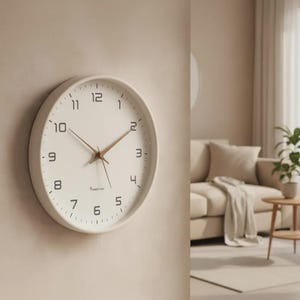 Puede incluir: Un reloj de pared redondo con esfera blanca, marco blanco y números arábigos negros. El reloj cuenta con manecillas finas de metal dorado para las horas, minutos y segundos. El texto "HARVEST VEE" está impreso en letras negras bajo el centro.