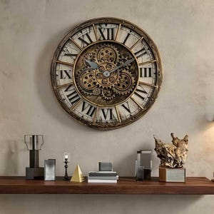 May include: A large, round wall clock with a vintage, industrial design. The clock features Roman numerals, a gold-colored frame, and visible gears in the center. The clock is mounted on a neutral-colored wall above a wooden shelf with decorative objects.